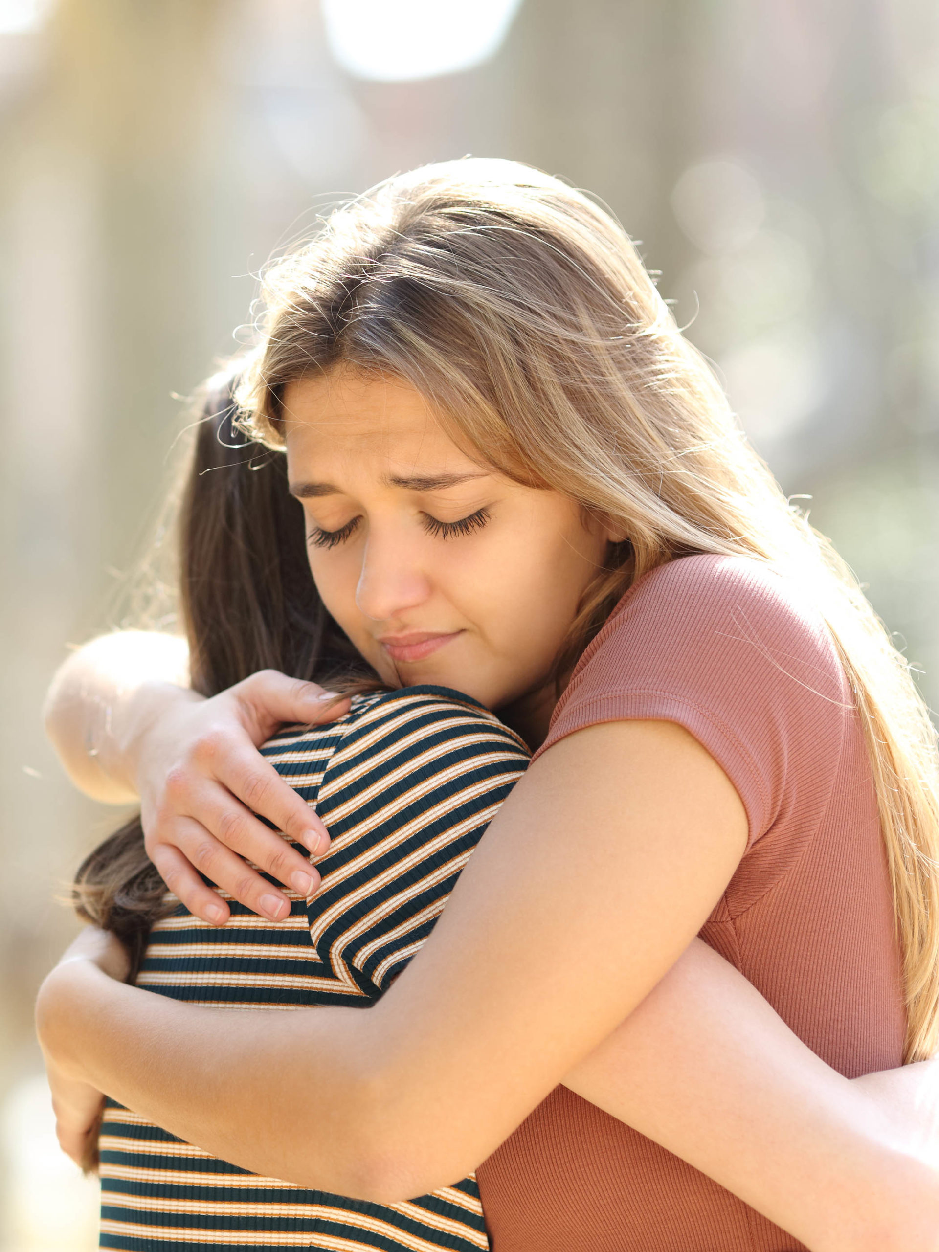 teen girl consoling her upset friend with a tight hug