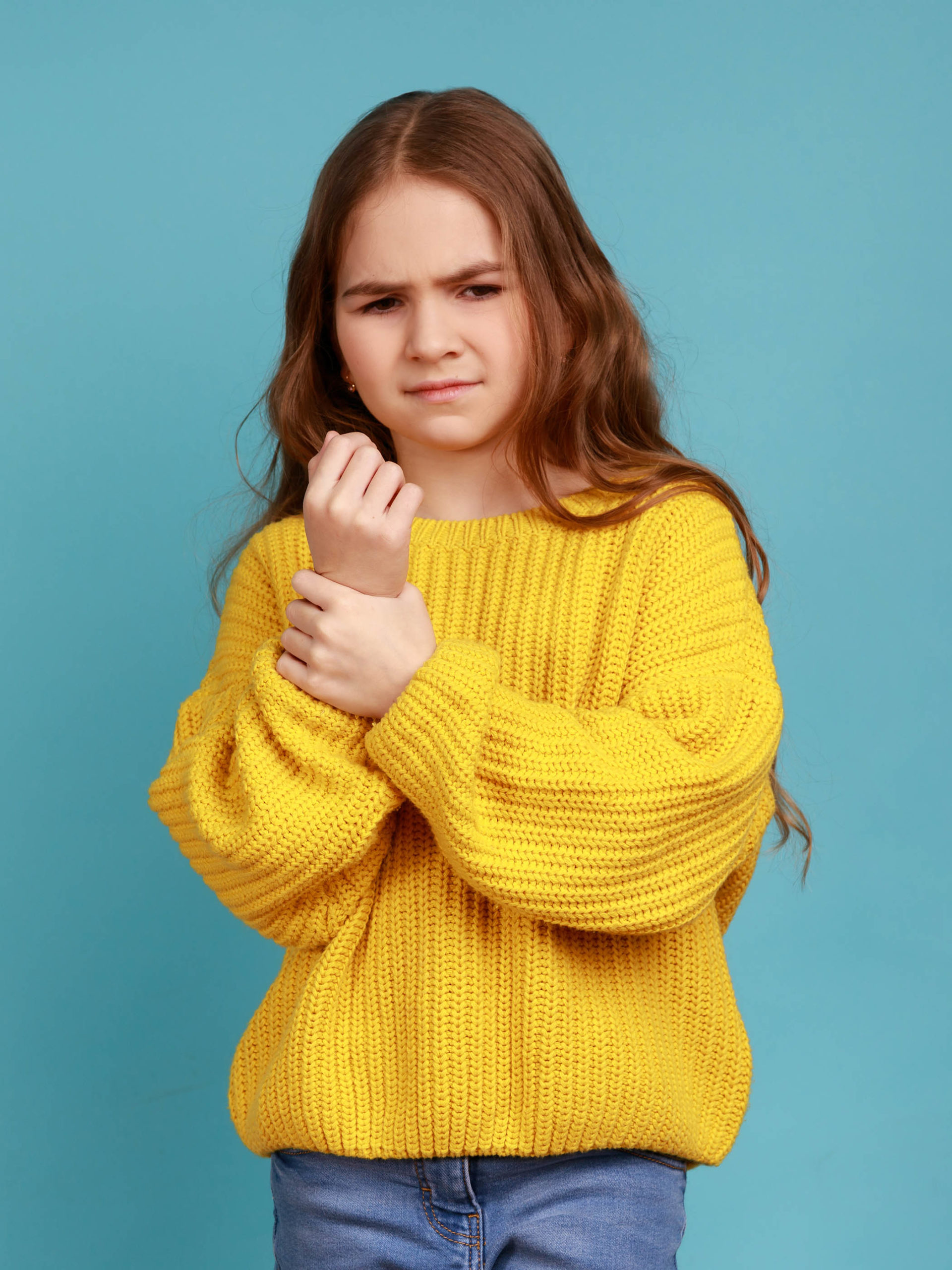 girl standing with grimace of pain, touching sore wrist