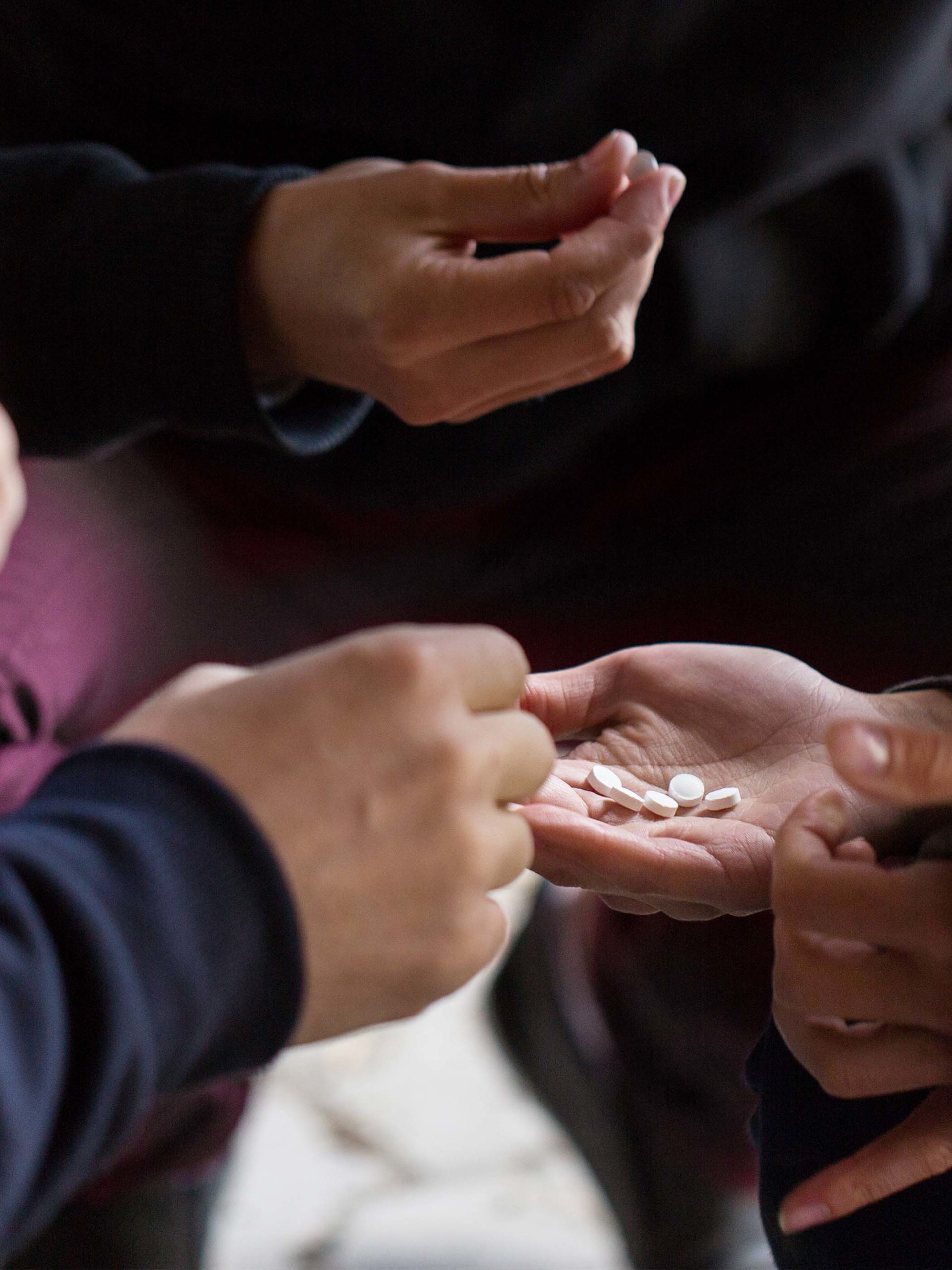 multiple hands take pills from a hand full of medications