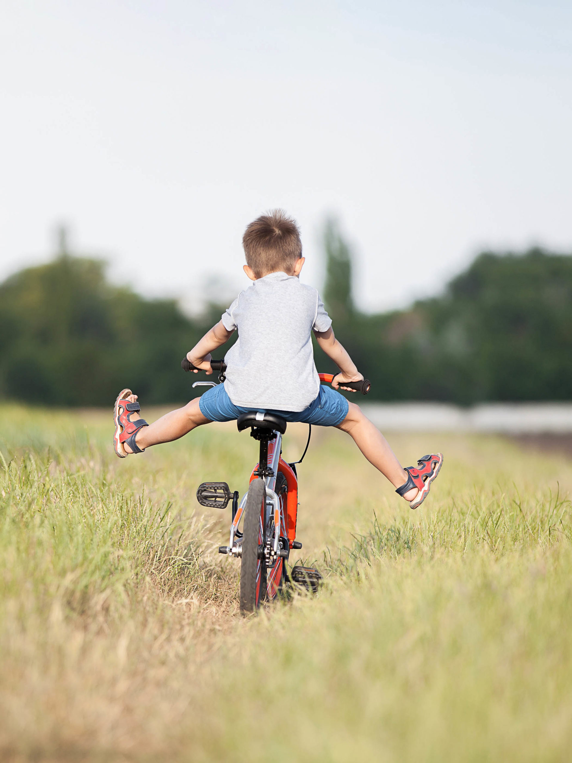 boy rides his bike through a meadow lifting his feet off the pedals