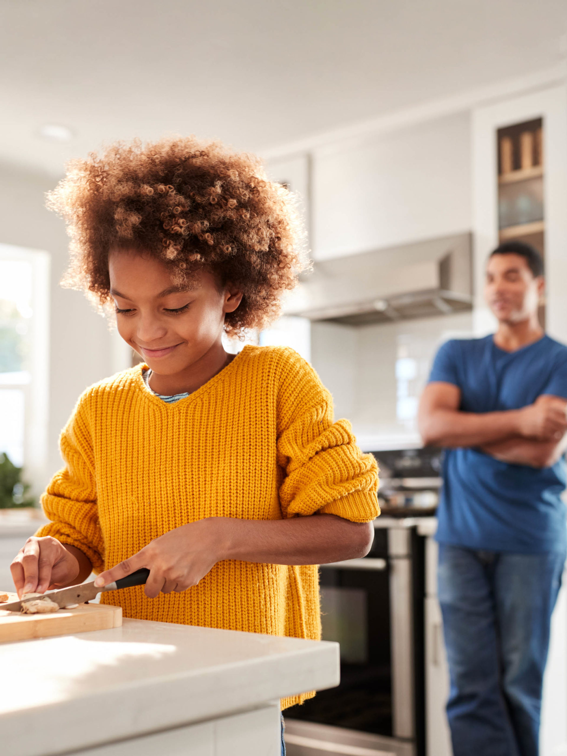 girl chopping food on counter while dad supervises her