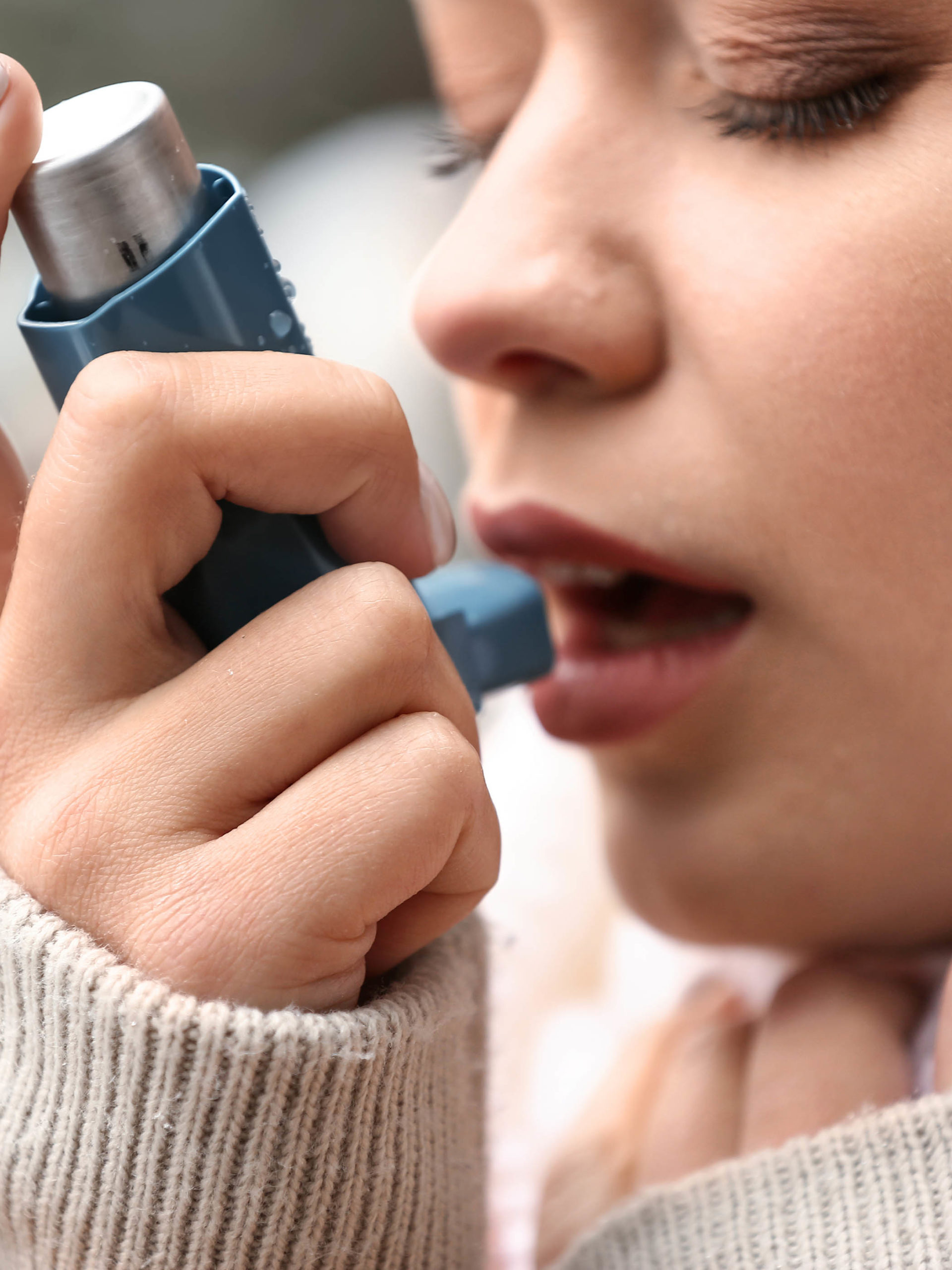 Young woman with inhaler having asthma attack outdoors