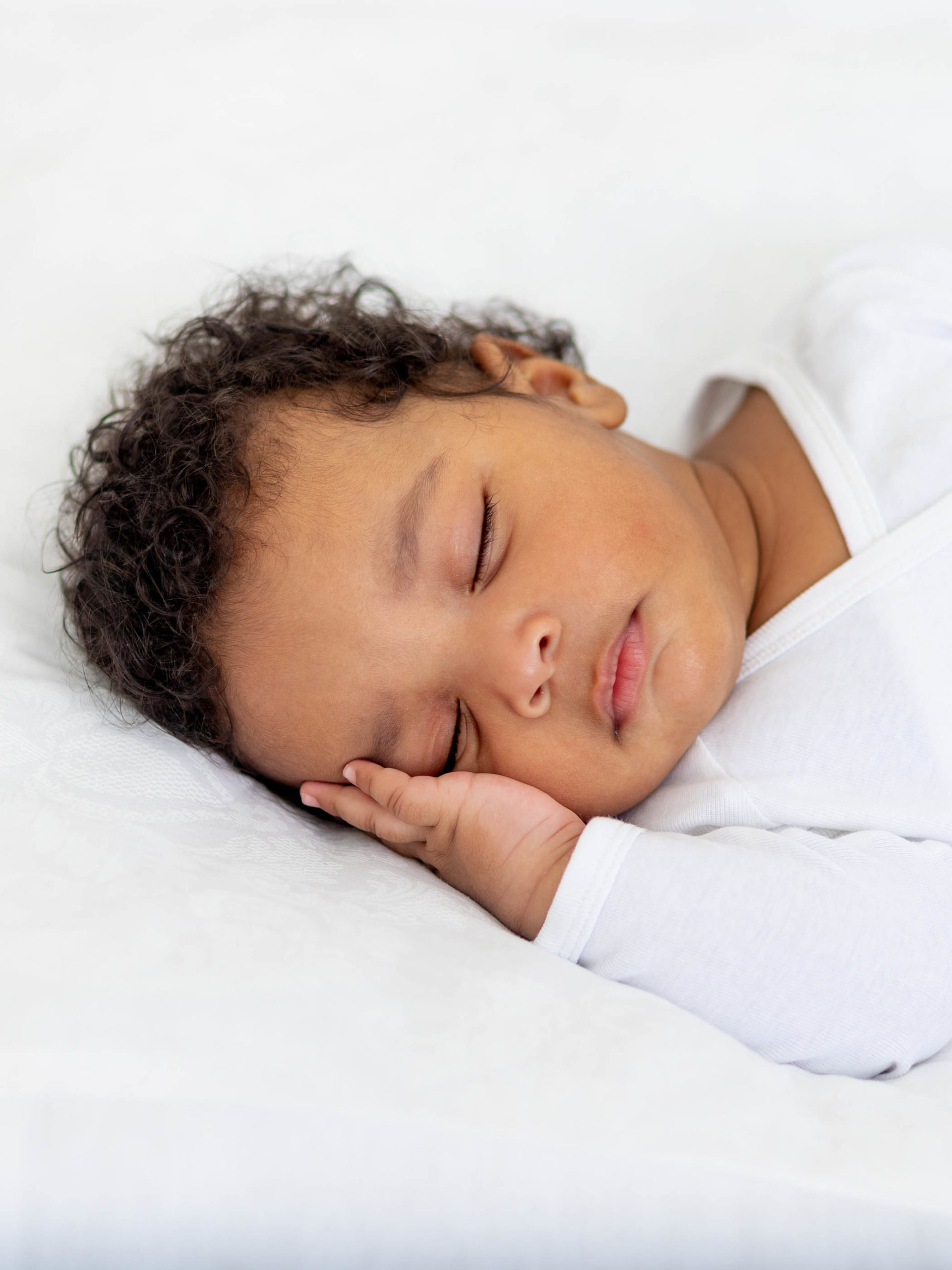 baby sleeps on a white bed at home with her hand folded under her cheek