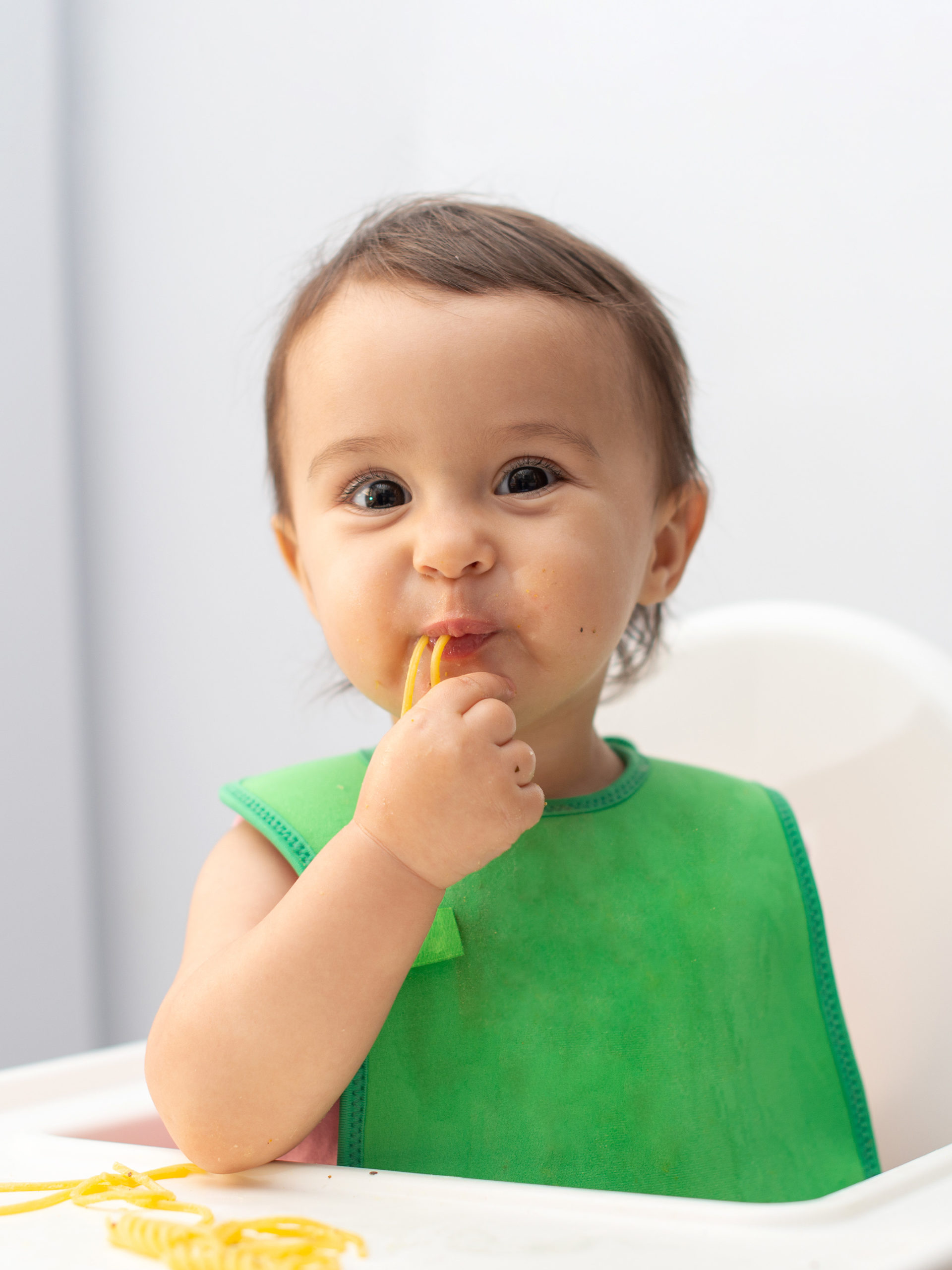 Baby sitting in high chair eating pasta