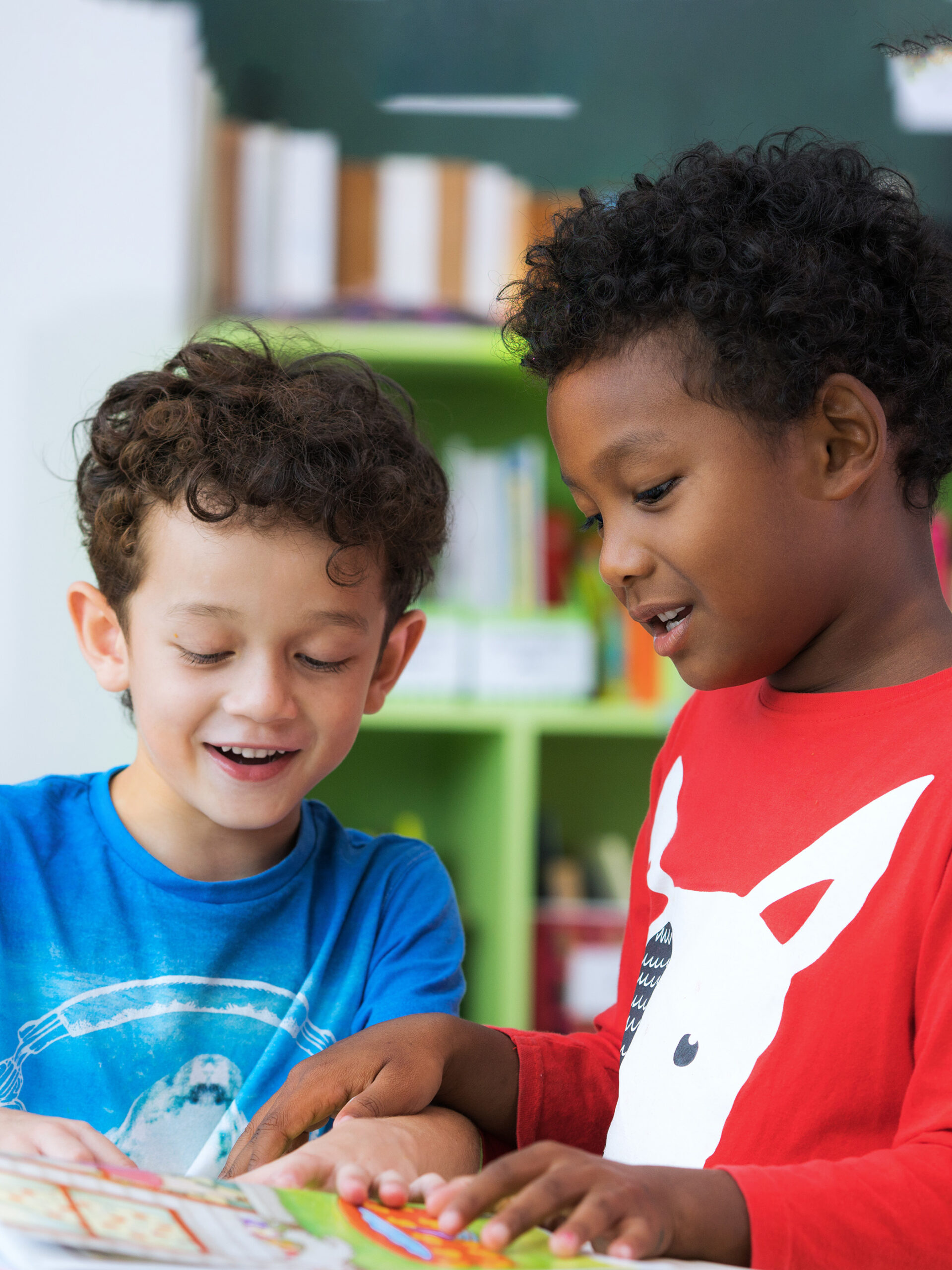 Two kids smiling and looking at a book together