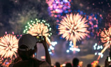 The back of a girl in a baseball cap filming a fireworks display on her mobile phone