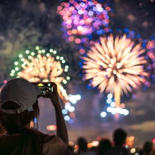 The back of a girl in a baseball cap filming a fireworks display on her mobile phone