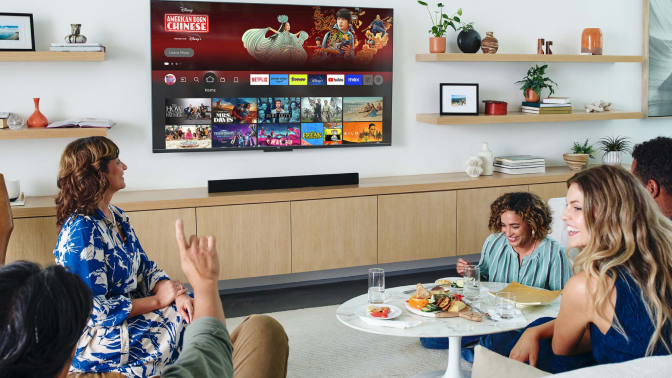 Four people sitting in living room with snacks and TV on wall with streaming apps on screen