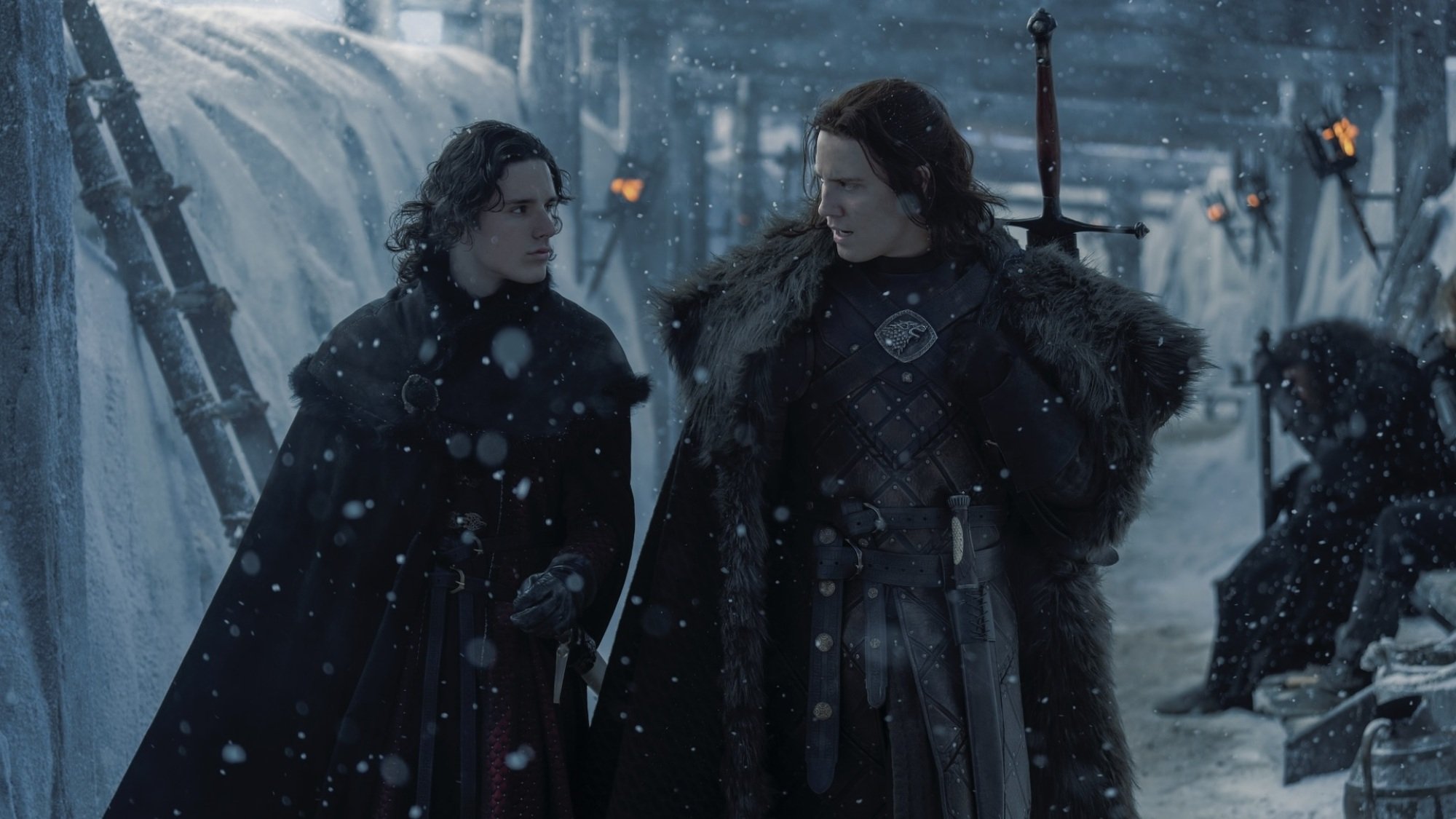 Jacaerys Targaryen and Cregan Stark walk along the snowy top of the Wall, wearing black fur cloaks.