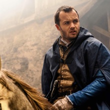 Matthew Shardlake from "Shardlake" rides a horse while wearing a blue cloak.