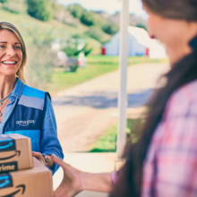 an amazon delivery woman handing amazon boxes to a woman in a pink flannel shirt on a doorstep