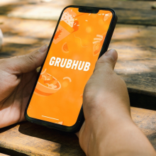 Girl in the park holding a smartphone with GrubHub food ordering and deliveryapp on the screen. Rustic wooden table. Rio de Janeiro, RJ, Brazil. July 2022.