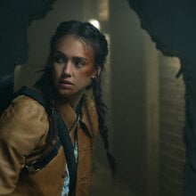 A woman with a bruised face creeps through a dark, abandoned building.