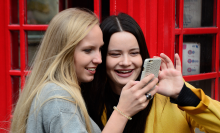 Two young women crowd together to look at a phone screen.