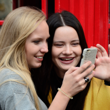 Two young women crowd together to look at a phone screen.