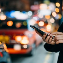 A person holds a phone while cars line up in the street behind them.