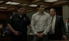 A man in a courtroom is led by a police officer.