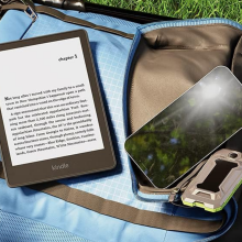 A Kindle Paperwhite sitting on a backback next to a smartphone