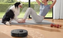 A woman does pilates with her dog while the eufy robot vacuum cleans pet hair