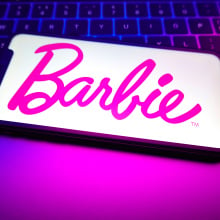 A Barbie logo is displayed on the screen of a smartphone.