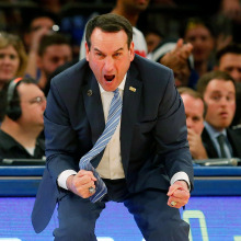 Duke head coach Mike Krzyzewski of the Duke Blue Devils leans forward, apparently shouting, with fists clenched. 