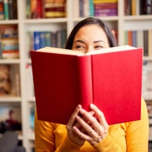 A woman poses with a book in front of a book shelf