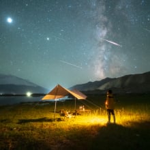 a person standing at a campsite as meteors streak overhead