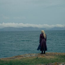 A woman stands on the edge of a large body of water, facing away from the camera.