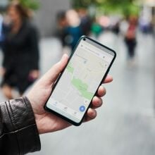 Detail of a man holding up a smartphone with the Google Maps app visible on screen.