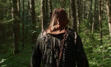 A man wearing a mask is seen from behind as he walks through the woods.