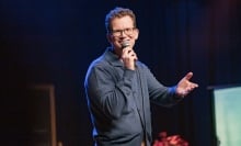 Hank Green performs stand-up onstage in a blue button-up sweater.