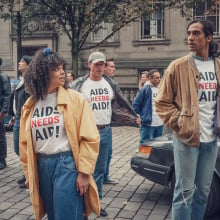 Lydia West as Jill Baxter and Nathaniel Curtis as Ash Mukherjee wearing T Shirts with the slogan "AIDS needs AID!"