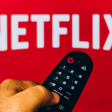 Hand holding a remote in front of a Netflix logo.