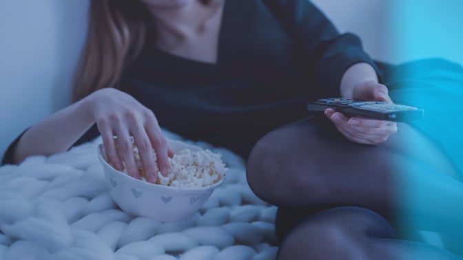 Person, neck down, with one hand in popcorn bowl and other hand holding remote