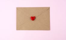 A brown envelope with a red heart on top of it, on a pale pink background. 