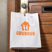 a white paper bag with a grubhub logo hangs on the doorknob of a front door