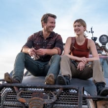Tyler (Glen Powell) and Kate (Daisy Edgar-Jones) in a still from Twisters. They are sitting on the hood of a truck.