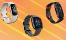 three fitbit fitness trackers sit on an orange background with white streaks