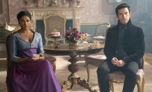 A man and woman in Regency attire, sitting several feet apart while she drinks tea; still from "Bridgerton."