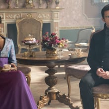 A man and woman in Regency attire, sitting several feet apart while she drinks tea; still from "Bridgerton."