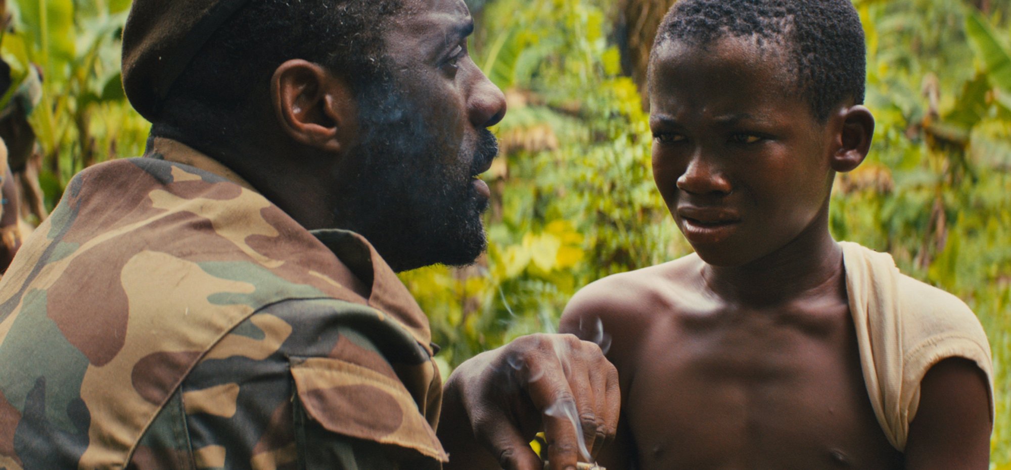 Closeup of an adult man in military fatigues and a small child; still from "Beasts of No Nation."