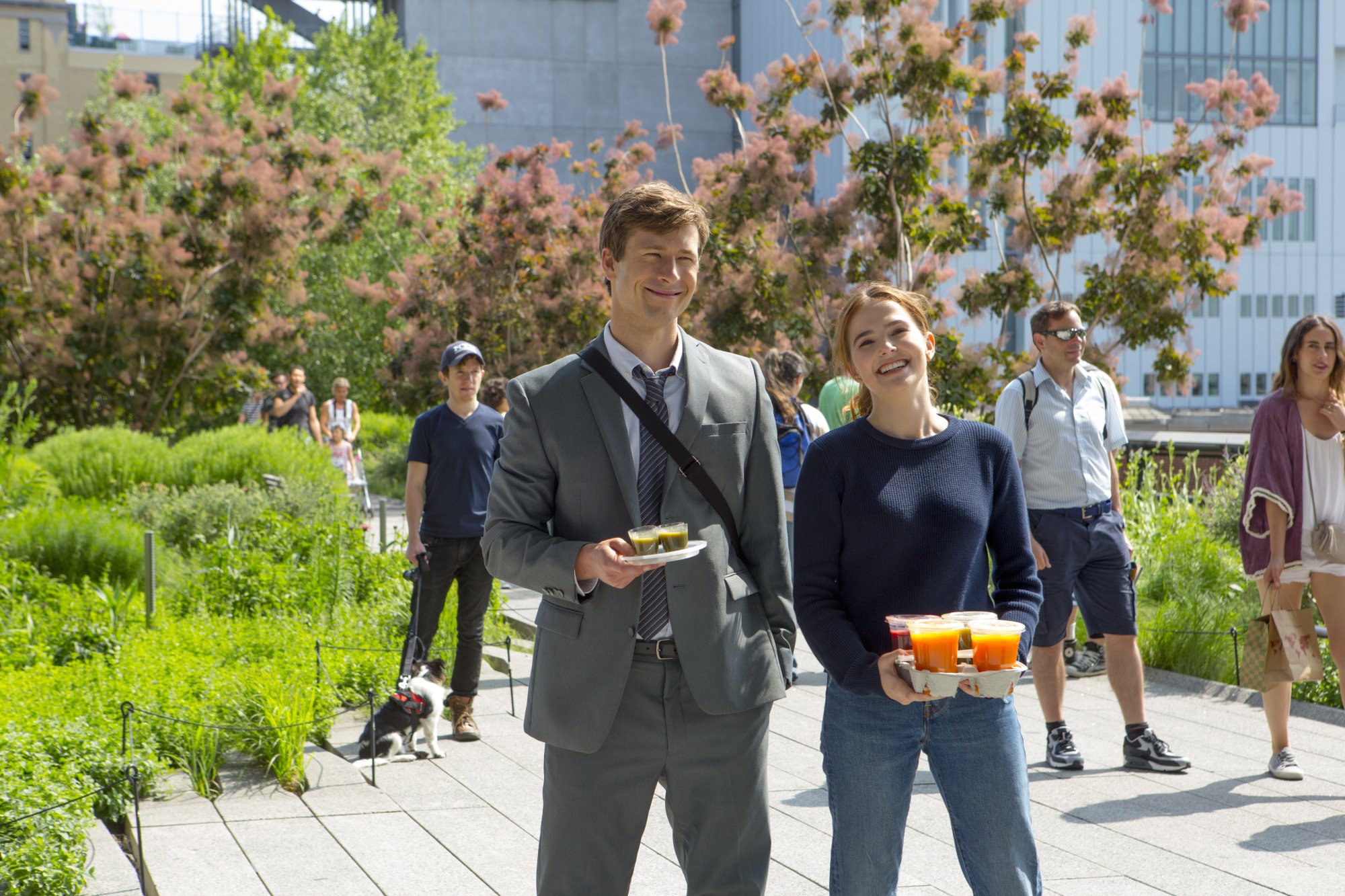 Zoey Deutch and Glen Powell stand next to each other on a path in "Set It Up."