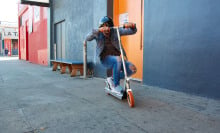 A helmeted person crouch on a scooter in front of colorful garages.