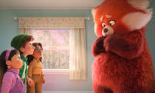 Three young girls stand at one end of a small room, looking at the giant red panda standing at the other end.