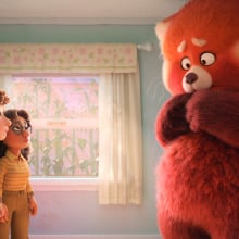 Three young girls stand at one end of a small room, looking at the giant red panda standing at the other end.