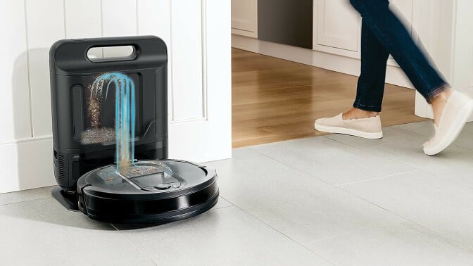 a robot vacuum is at its dock, emptying, while someone walks by on the right side