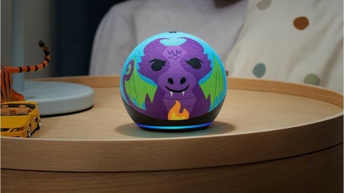 an amazon echo dot kids circular speaker with a colorful face of a dragon sits on a wood nightstand