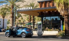 A blue car in front of a Starbucks plugged into a charging station.