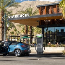 A blue car in front of a Starbucks plugged into a charging station.