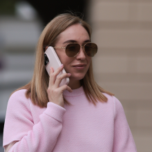 A woman wearing a pink sweater and sunglasses holds a phone to her ear.